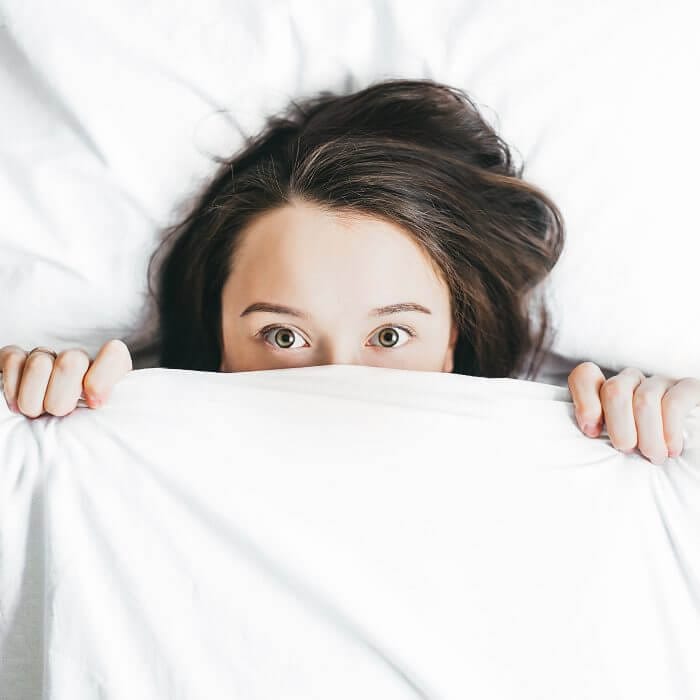 woman hiding under sheet who is wondering what hormone imbalance is causing her acne