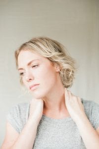 woman holding her neck looking tired because her thyroid is not working due to hypothyroid