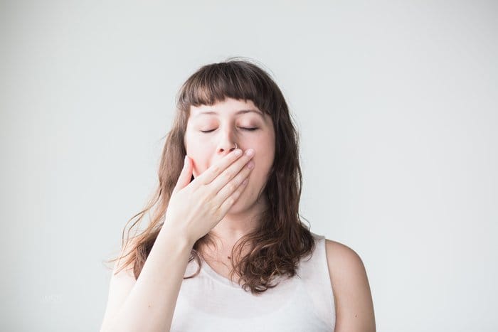 picture of a woman covering her mouth because she is yawning because she wakes up tired due to adrenal fatigue or HPA axis dysfunction