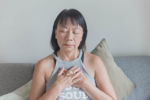 picture of a woman holding her hands to her chest to calm her anxiety with meditation after having a hot flash at menopause