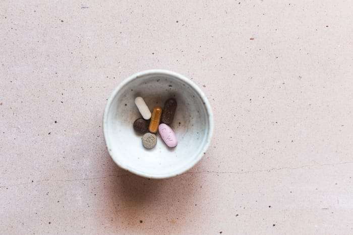 picture of a bowl with glutathione supplements, vitamin C, vitamin E, and liver detoxification supplements in it on a pink background